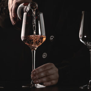 Sommelier pouring rose wine into glass at wine tasting in winery, bar or restaurant. Dark background