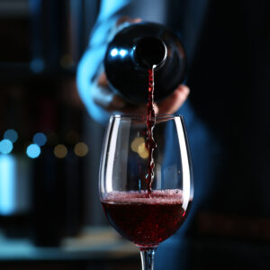 Bartender pouring red wine from bottle into glass indoors, closeup